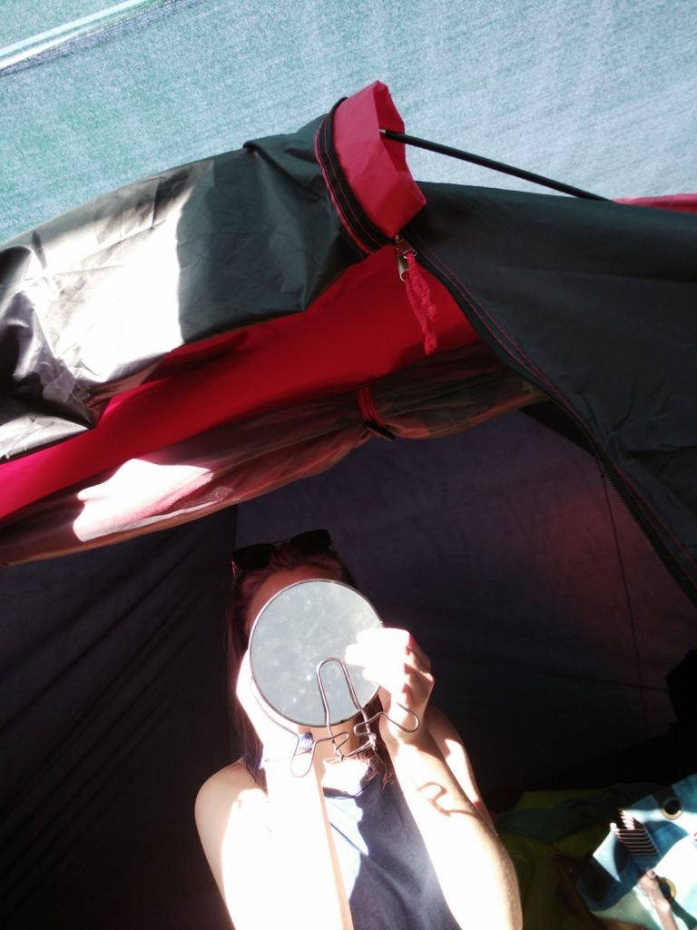 A girl doing her makeup in the mirror in a tent